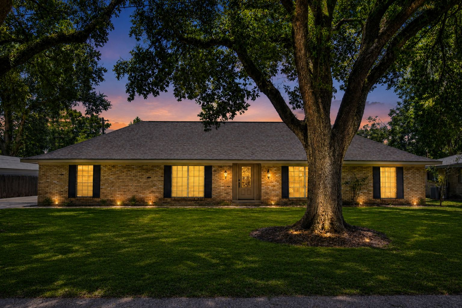 Single-story brick home and oak tree at twilight